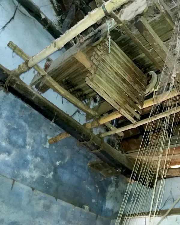 The timber frame of a handloom seen from below, warp threads running through it.
