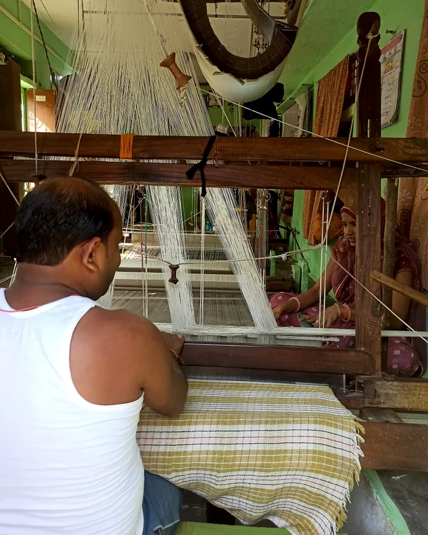 A weaver at the bench, a part-woven sari stretched in front of him.