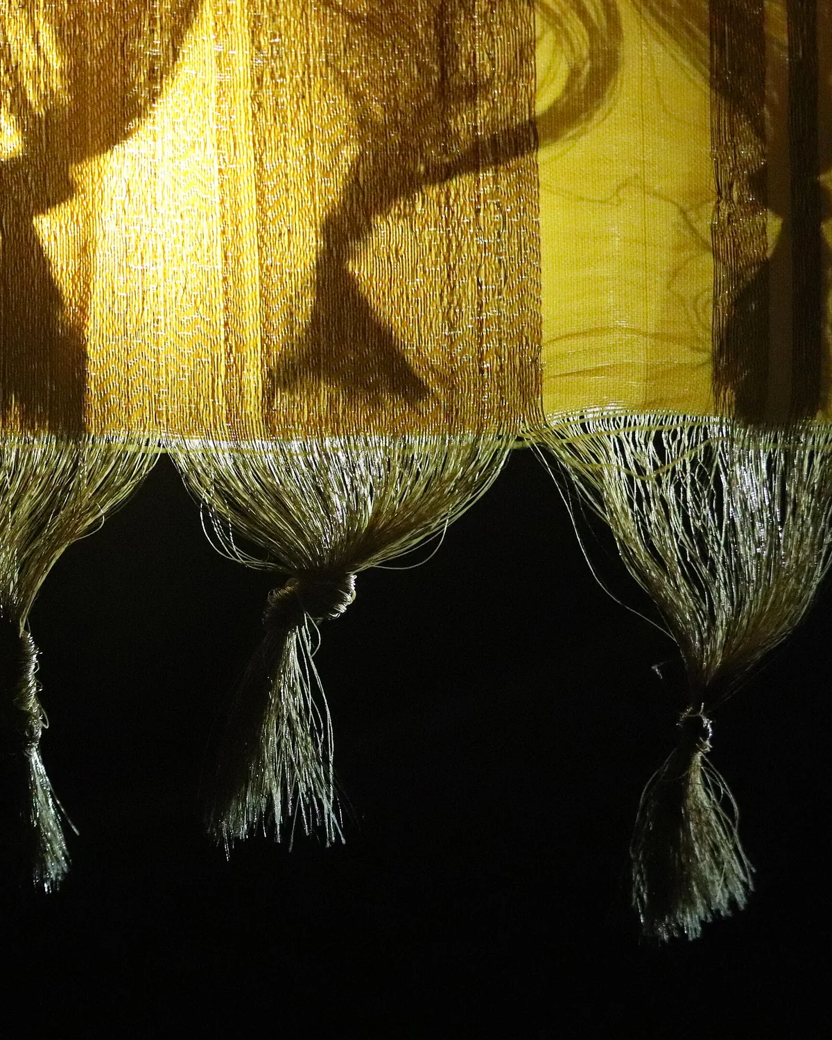 Gold kuchu knots tied along the end of a sari, lit against a dark ground.