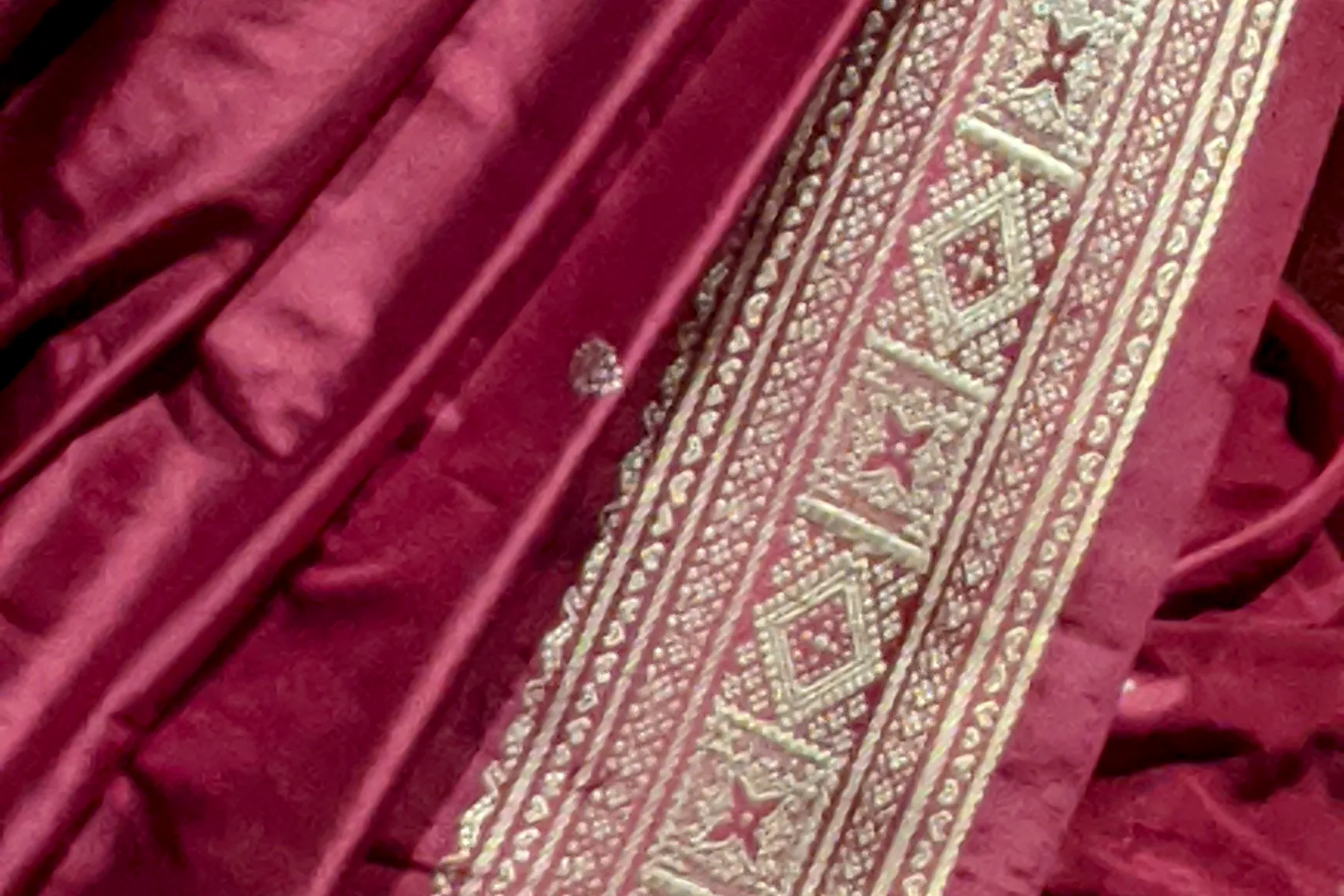 A deep madder handloom sari folded to show the fine woven border running along its edge.