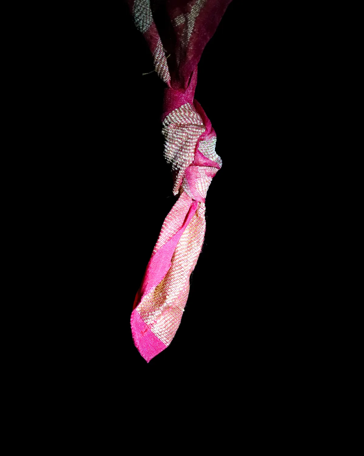 A knot tied into the end of a sari, lit against a dark ground.