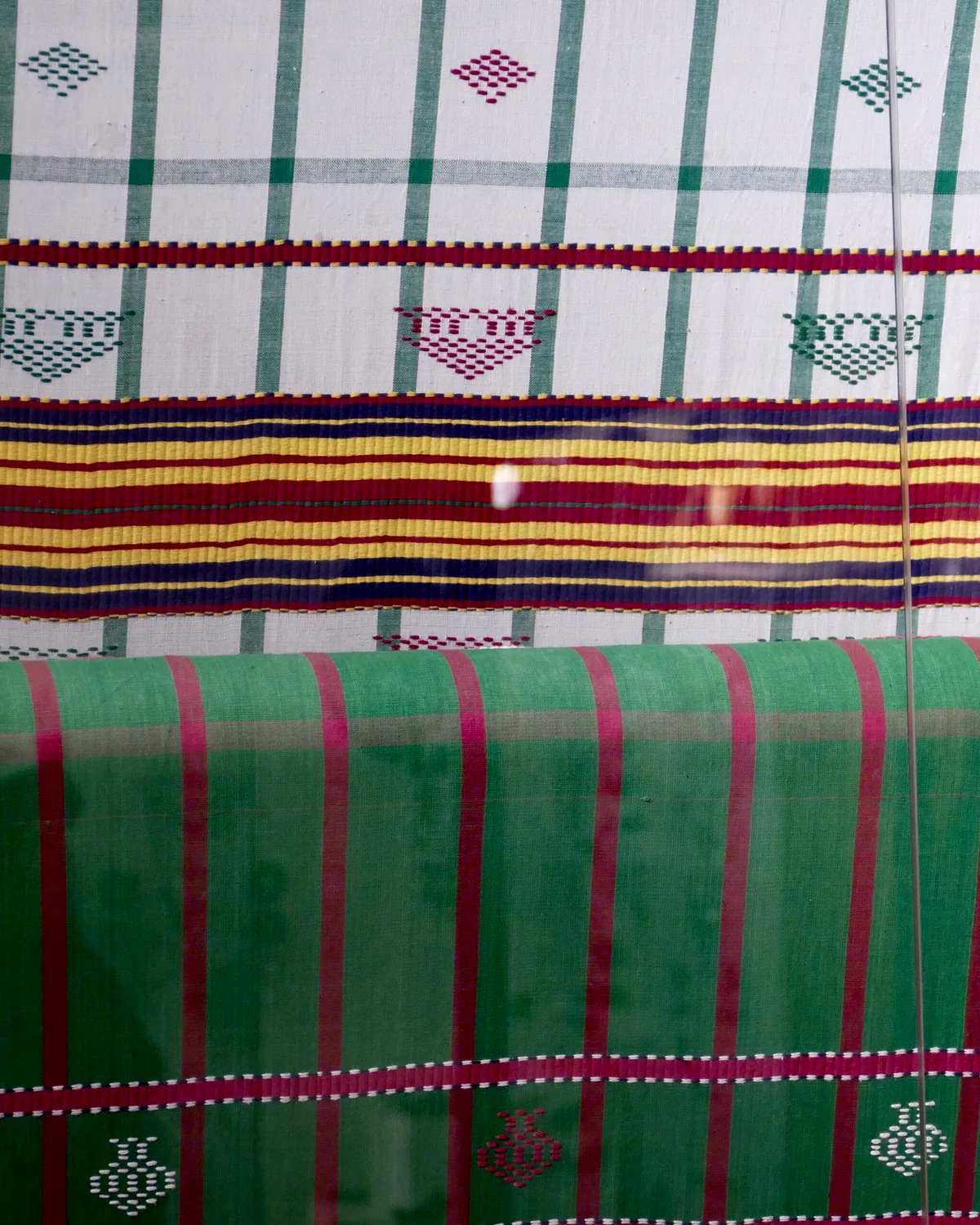 Woven cloth in green and madder stripes, still on the loom.