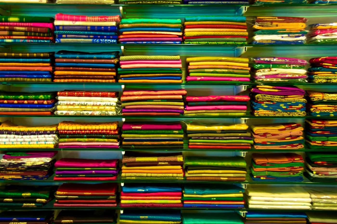 Folded saris stacked by colour on the shelves of a cloth shop.