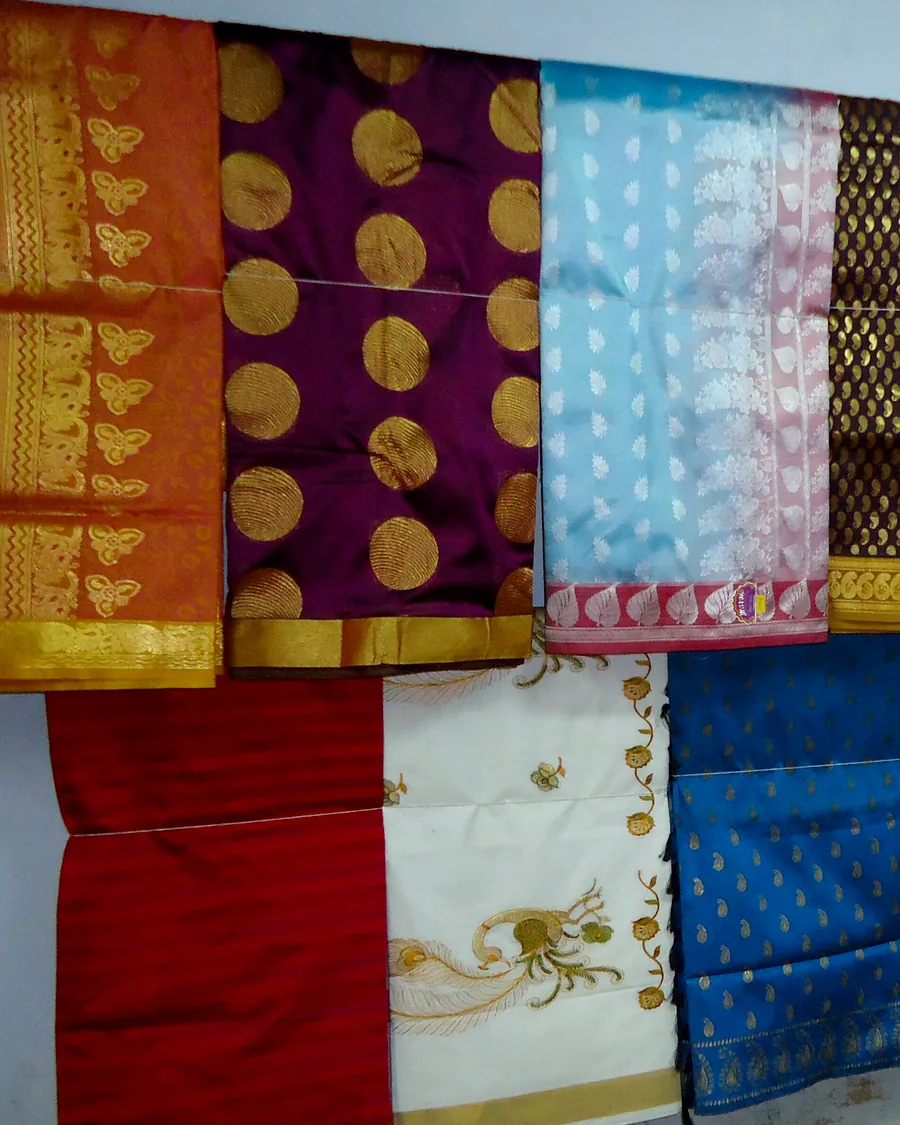 Kanchipuram silk saris hung in a row, each with a heavy woven gold border.
